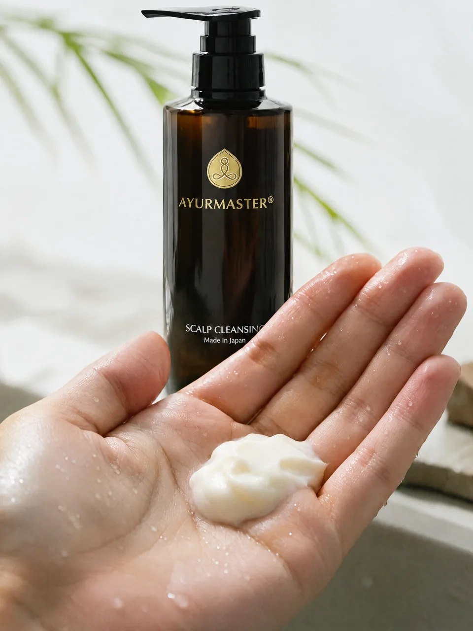 A wet palm holding Scalp Cleansing Shampoo cream in front of the AYURMASTER bottle