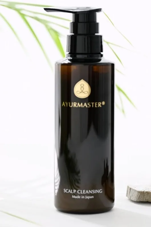 A bottle of AYURMASTER Scalp Cleansing Shampoo beside a palm leaf